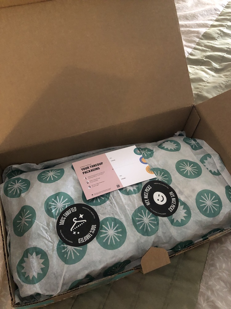 Opened ThredUp box with tissue paper and stickers that say "100% thrifted" and "Hey Nice Picks"